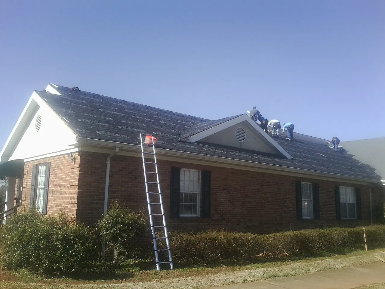 Crew tearing shingles off a brick ranch roof with a ladder set — Emergency Roof Repair work by our crew in Mount Hamilton