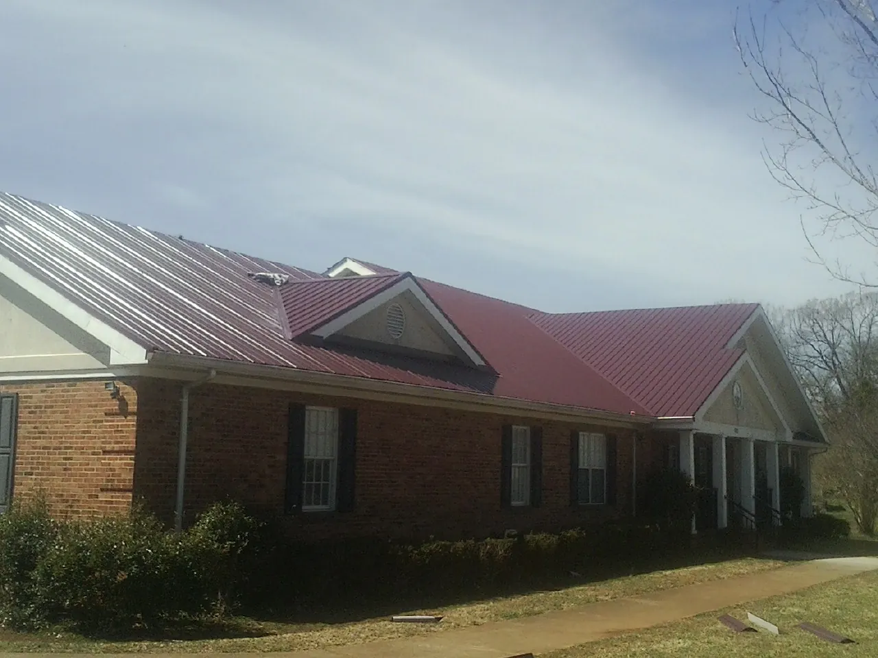 Red metal roof with gabled entries on a long brick building, from a Hail Damage Roof Repair job in Mount Hamilton